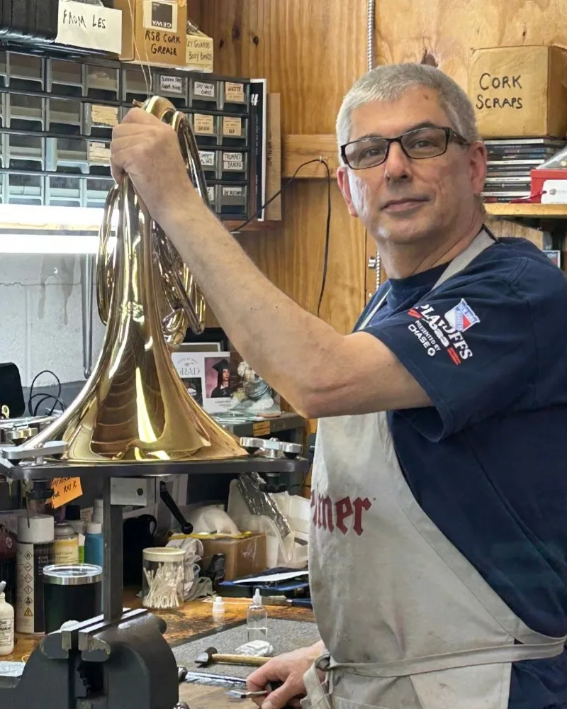 Gerry Falco at his bench, holding a brass horn he is working on